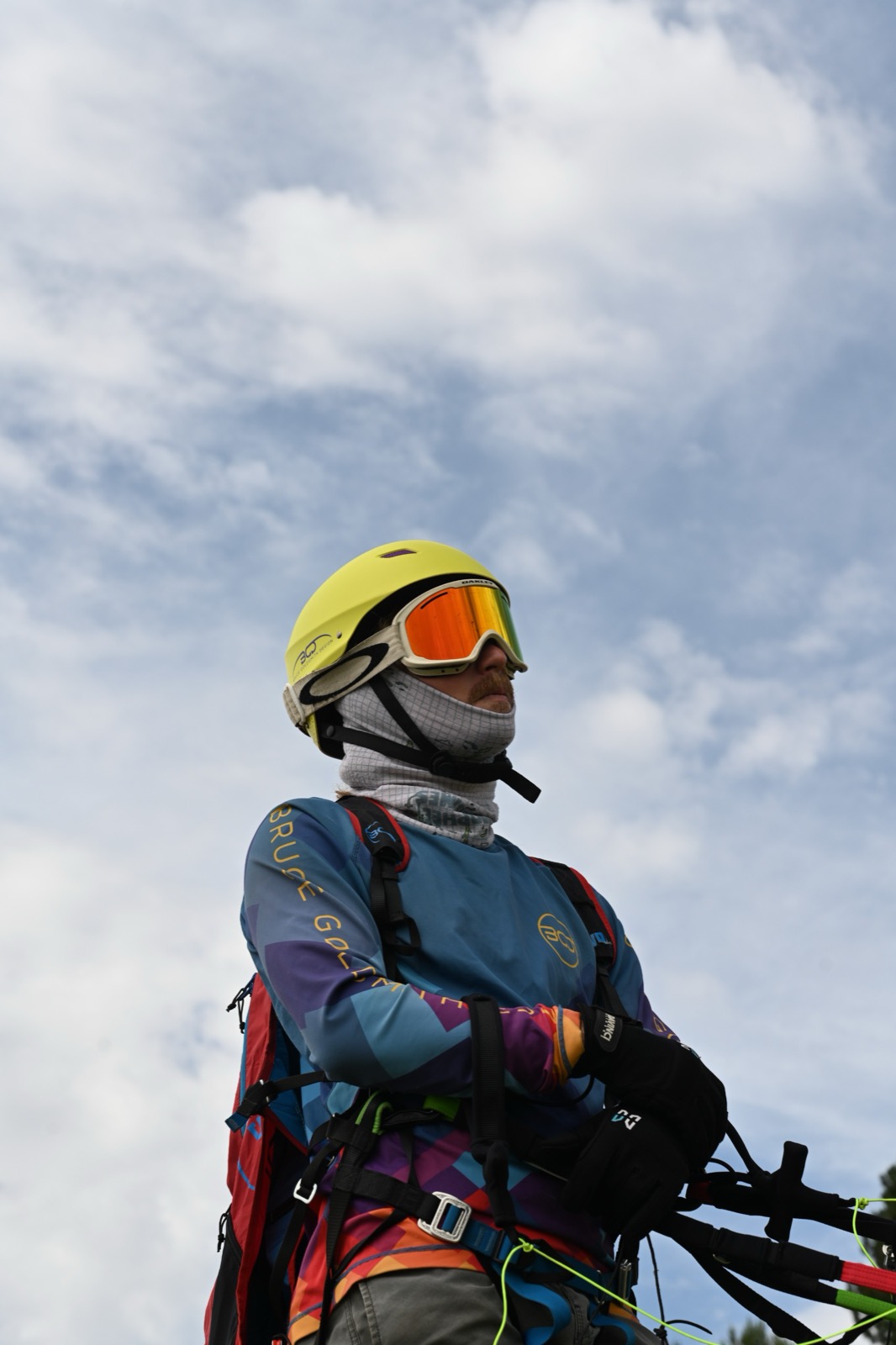 A paragliding pilot in a yellow helmet and mirrored goggles, geared up before takeoff